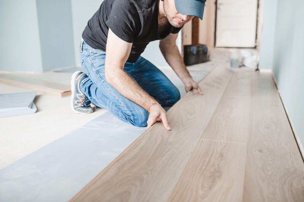 man installing floating flooring with expansion gap around perimeter